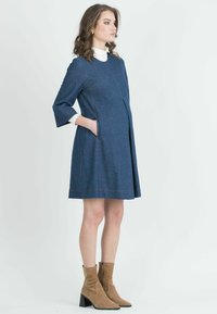 Denim A-linjainen mekko, jossa on kolmen neljänneksen hihat, sivutaskut ja erottuva oranssi ommel. Yhdistetty ruskeisiin nilkkabootseihin ja valkoiseen poolopaitaan.