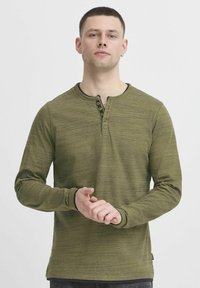 Žalia ilgomis rankovėmis henley marškinėliai su tekstūruotu audiniu, su juodais mygtukais voko ir rankogaliais, ir apvaliu iškirpimu.