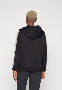 Felpa nera con cappuccio regolabile, caratterizzata da strisce laterali decorative bianche. Realizzata in tessuto solido con polsini e vita a costine.