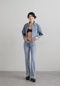 Šviesiai mėlyna džinsinė striukė su gėlių siuvinėjimu, derinama su žemais mėlynais džinsais. Po striuke matosi juodas naktinis liemenėlė, o platformos batai yra tamsūs.