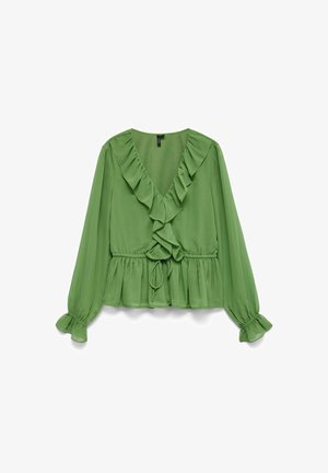 Zaļa blūze ar garām piedurknēm, V-veida kakla izgriezumu, volānu akcentiem un elastīgu jostas daļu. Iezīmē savilktas aproces un saistošu detaļu jostas daļā.