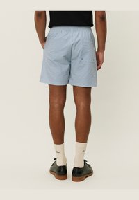 Lysblå og hvide stribede shorts med elastisk talje, sidelommer og baglomme samt en løs pasform. Sammen med sorte sko og beige sokker.