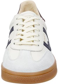 Zapatilla de cuero blanca con detalles en azul marino y capuchón de ante en la punta. Presenta cordones redondos, un cuello acolchado y una suela de goma texturizada.