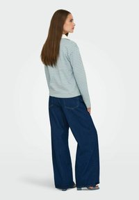 Camiseta de manga larga a rayas en azul claro y blanco, combinada con unos vaqueros de pierna ancha en denim oscuro. La modelo se encuentra de espaldas, mostrando el ajuste y el diseño.