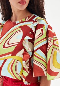 Top a maniche corte in tessuto colorato con dettagli arricciati, caratterizzato da schemi astratti in rosso, verde, blu e crema. Texture liscia.