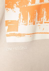 Beige kangas, jolla on oranssi ja valkoinen abstrakti rakennuskuvio ja kohokuvioitu "ONLY & SONS" -teksti suunnittelun alapuolella.