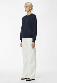 Sweatshirt blu navy con scollatura rotonda, maniche e orlo a costine, abbinato a pantaloni bianchi a gamba larga e sandali neri. Design semplice e casual.