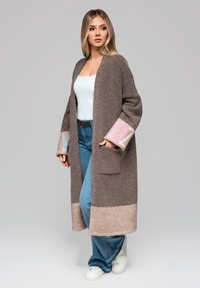 Cardigan lungo marrone in materiale morbido, con orlo e polsini beige chiaro decorati con motivi rosa e blu, due tasche laterali.