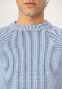 Light blue knitted sweater with a ribbed texture. Features a round neck and raglan sleeves, highlighting a structured and modern design.