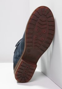 Niebieski zamszowy but z teksturowaną podeszwą z gumowymi wzorami zapewniającymi przyczepność. Podeszwa ma brązowy akcent i jest lekko zużyta.