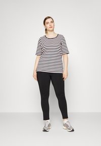 T-shirt de mangas curtas às riscas em rosa e azul marinho, combinado com leggings pretas e tênis atléticos prateados, de pé contra um fundo simples.