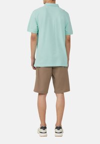 Polo-shirt à manches courtes vert menthe avec un col, associé à un short beige. Les chaussures sont blanches avec des accents gris ; la tenue est décontractée et relaxée.