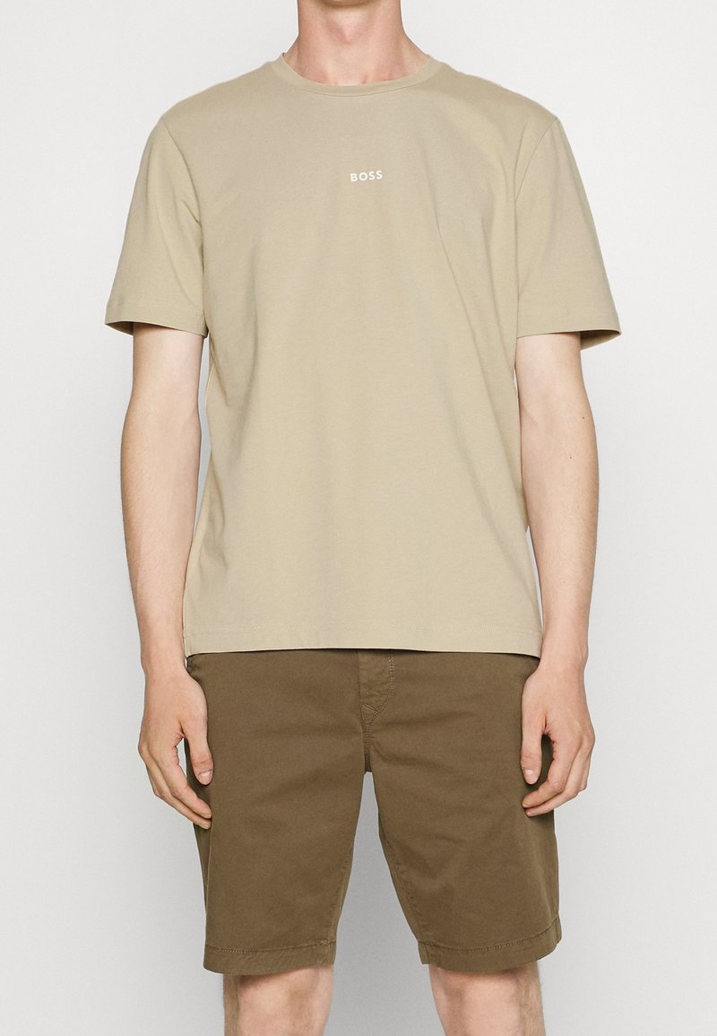 Béžové bavlněné tričko s krátkým rukávem a kulatým výstřihem, se středovým malým bílým logem "BOSS"; spárováno s hnědými šortkami.