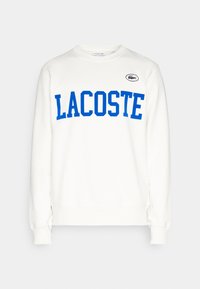 Vit sweatshirt med blå "LACOSTE" text, rund halsringning, lång ärm, ribbad mudd och en liten logotypaccent på övre vänster sida.