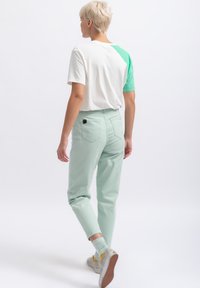 Muntgroene broeken met een relaxte pasvorm, gecombineerd met een wit en groen kleurblok T-shirt. Casual sneakers maken de outfit compleet.