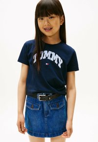 Marinen t-shirt i bomuld med hvid "TOMMY" skrift, parret med en blå denimnederdel med frontlommer og et sort bælte.