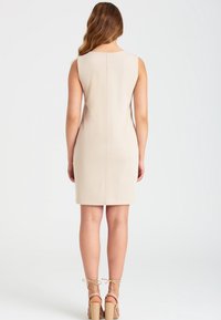 Beige ärmlös klänning med rak silhuett, med en söm i ryggen. Matchad med nakna högklackade sandaler med ankelband.