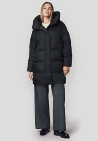 Czarna kurtka puchowa z kapturem, z pikowanym wzorem, zapięciem na napy z przodu oraz dwoma bocznymi kieszeniami. Zestawiona z szarymi spodniami z szerokimi nogawkami.