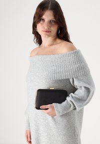 Sivi pleteni pulover s nepodprtim ramom in rebrasto strukturo, kombiniran s črno torbico na ramah z zlatim zaponko.