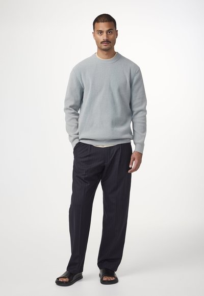 Helles blaus strukturiertes Sweatshirt, schwarze streifenbedruckte Hose und schwarze Sandalen. Einfaches Design mit lockerer Passform und Rundhalsausschnitt.