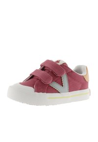 Sneaker in tela rosa con accenti grigi, due cinturini con chiusura a velcro, suola in gomma bianca e punta arrotondata. Presenta un piccolo dettaglio a forma di fiore sulla linguetta.