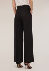 Zwarte wijde broek met een gladde textuur, voorzien van zijzakken en een op maat gemaakte pasvorm, gecombineerd met gespsandalen met hak.