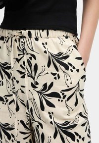 Lichte katoenen broek in beige met zwarte bloemenpatronen, voorzien van een elastische tailleband en zijzakken voor comfort en functionaliteit.