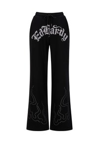 Zwarte trainingsbroek met een trekkoord in de taille en een groot zilverkleurig "Ed Hardy" logo. Versierd met studs in vlampatronen langs de benen.