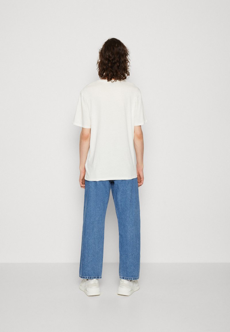 T-shirt bianco in cotone con maniche corte, vestibilità rilassata. Abbinato a jeans a gamba larga azzurri, con orli sfilacciati e sneakers bianche.