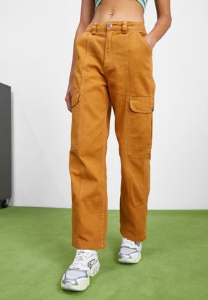 Cargo pants in a mustard yellow color, made of durable fabric. Features include multiple side pockets and a relaxed fit with a straight leg design.