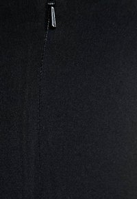 Gros plan sur un tissu noir avec une couture verticale et un curseur de fermeture éclair argenté partiellement visible en haut.