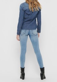 Jeansskjorta i djupt blått med långärmade ärmar, utrustad med klassisk krage och sydda detaljer. Kombinerad med ljusblå skinny jeans och svarta ankelboots.