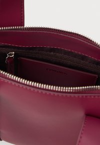 Unutrašnjost burgundske kožne torbe sa zatvaranjem na patentni zatvarač, koja sadrži malu zipersku džepu i glatku teksturiranu pregradu za kartice.