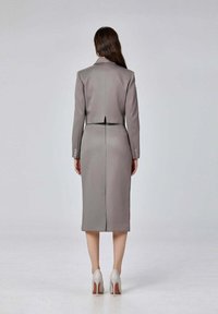 Costume gris ajusté avec une silhouette cintrée, comprenant un blazer court et une jupe au genou. Tissu lisse avec des détails en boutons et un dos fendu.