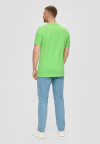 Groen T-shirt met korte mouwen en een ronde halslijn, gecombineerd met lichtblauwe jeans en witte sneakers, gezien vanaf de achterkant.