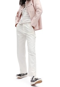 Vita bomullbyxor med avslappnad passform, tillsammans med en rosa kanvasjacka och randig skjorta, kompletterat med svartvita sneakers.