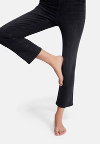 Svarta denim cropped jeans med rak bendesign, med rå avslutning och subtila blekningar, visade med en bar fot mot en vit bakgrund.
