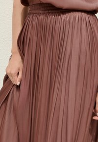 Gonna lunga plissettata in morbido tessuto rosa polveroso. Presenta una cintura elastica arricciata e una consistenza leggera e fluida per il movimento.