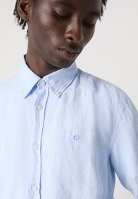 Lichtblauwe button-up shirt van zacht fabric, met een klein geborduurd logo op de borst, puntige kraag en witte knopen.