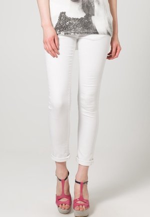 Weiße Skinny-Jeans mit hochgekrempelten Säumen, kombiniert mit rosa High-Heel-Sandalen mit Cut-Out-Details und Plateau-Sohle.