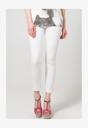 Vaqueros blancos ajustados con puños doblados, combinados con sandalias de tacón alto rosas con detalles recortados y suela con plataforma.