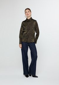 Leopard print button-up shirt in dark green and black; paired with wide-leg dark denim jeans and black heeled boots.