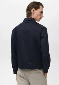Marine-kleurige katoenen jas met een ronde kraag, knoopmanchetten en een recht model. Voorzien van een rugnaad en minimale details.