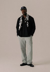 Black long-sleeve shirt, zippered neck, gray textured wide-leg pants, patterned scarf, and black shoes. Gray background highlights outfit.