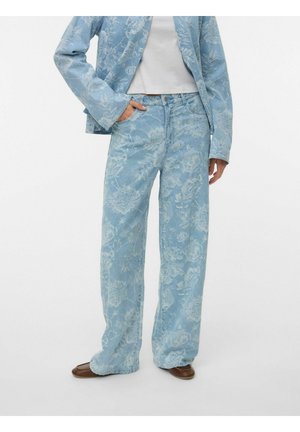 Luźne jasnoniebieskie dżinsy z delikatnym kwiatowym wzorem, noszone z dopasowaną kwiatową kurtką, białym topem i brązowymi płaskimi butami.