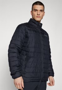 Giacca puffer blu navy con collo alto, design trapuntato orizzontale e tasche con zip. Realizzata in tessuto leggero e isolato.