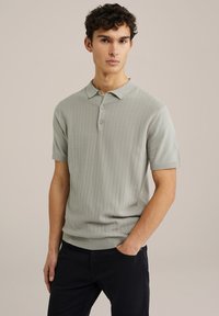 Polo shirt gri deschis, cu mânecă scurtă, cu o textură dublată, cu plastron cu trei nasturi și un guler clasic. Purtați cu pantaloni închiși.