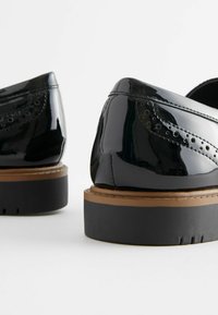 Scarpe in pelle verniciata nera con dettagli a punta e una suola spessa nera, caratterizzate da un'accattivante finitura marrone attorno al gambetto.