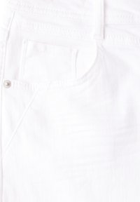 Tela de mezclilla blanca con una textura de finas estrías. Presenta un pequeño bolsillo frontal y herrajes metálicos plateados en la cinturilla.