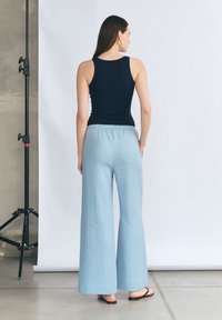 Czarny bezrękawnik w połączeniu z jasnoniebieskimi spodniami typu wide-leg, posiadającymi elastyczny pasek w talii i teksturowany materiał. Czarne sandały dopełniają całość.